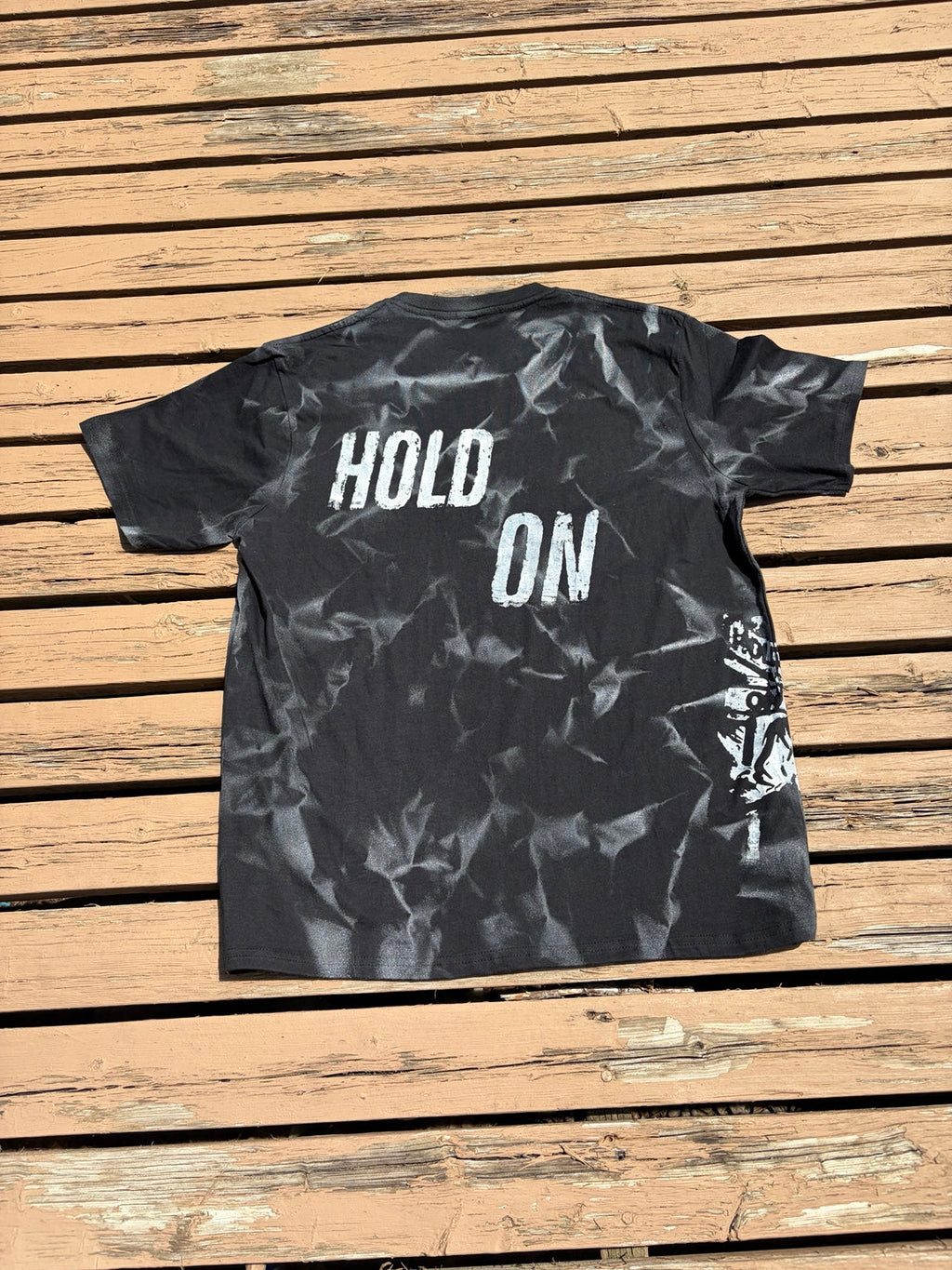Back of Hold On Shadow Graphic Tee laid flat on wooden deck