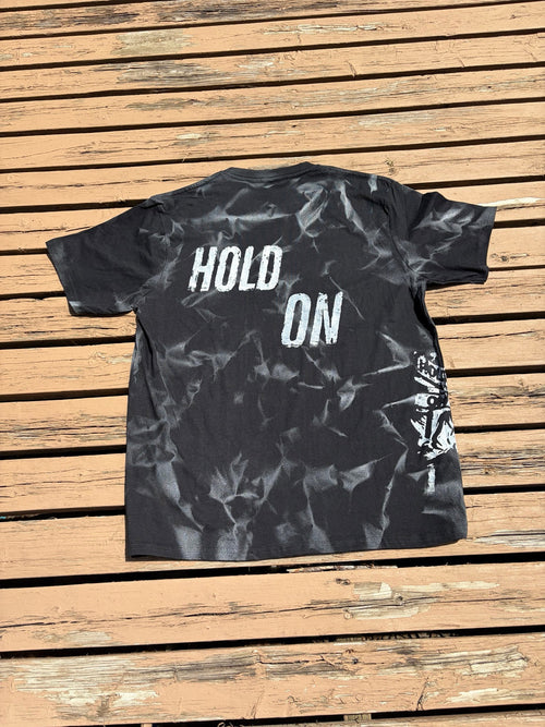 Back of Hold On Shadow Graphic Tee laid flat on wooden deck