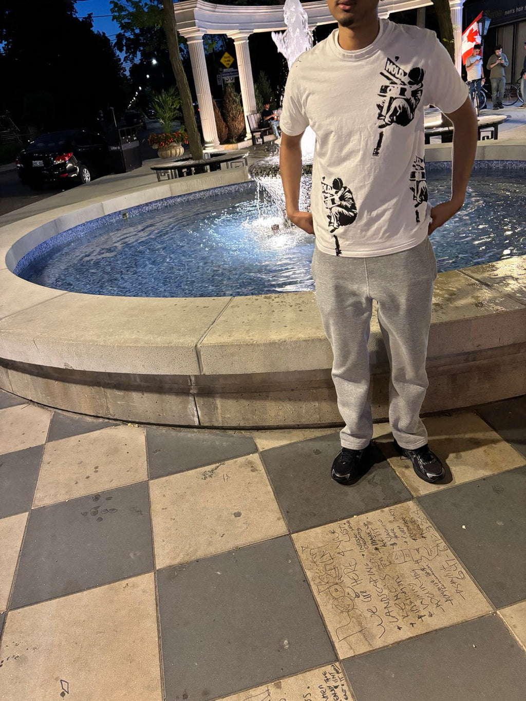 Model wearing the Hold On White Graphic Tee near a fountain at night