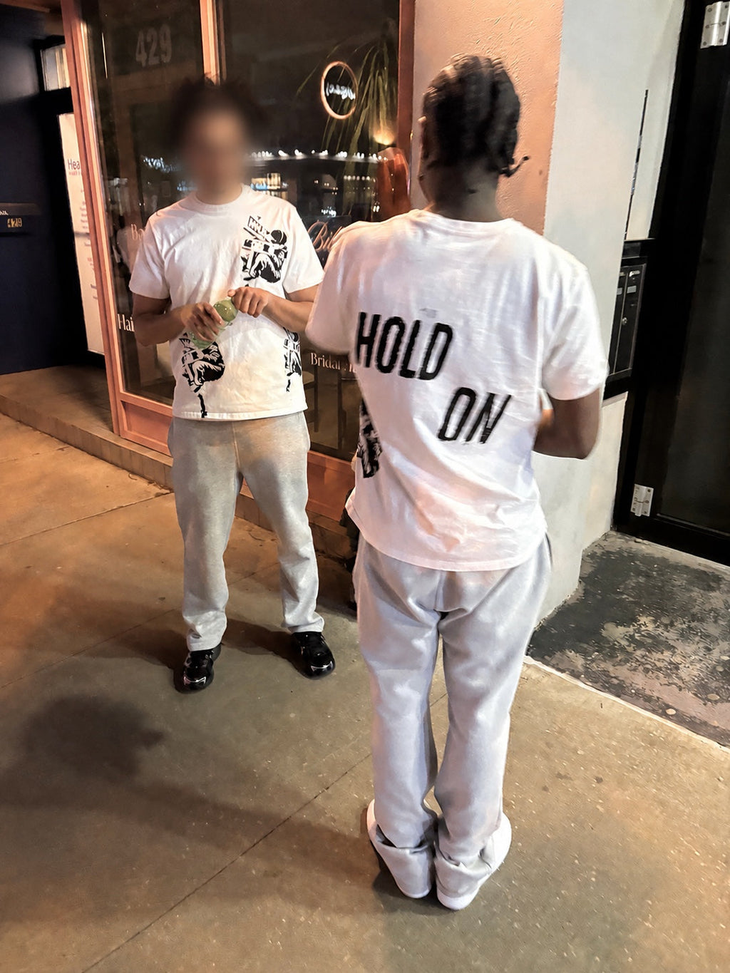 Two models wearing the Hold On White Graphic Tee at night with one face blurred