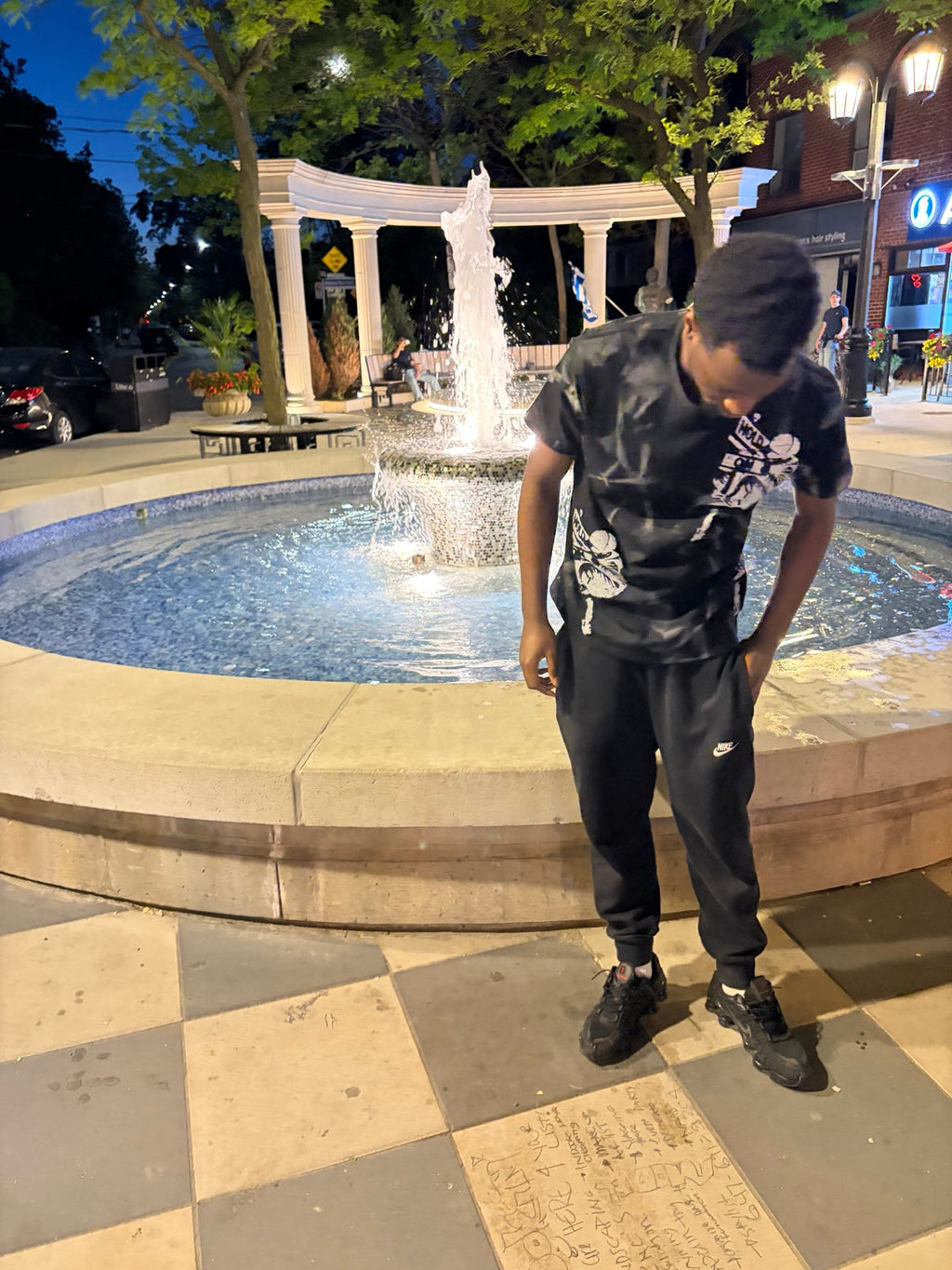 Front view of model wearing Hold On Shadow Graphic Tee by fountain at night